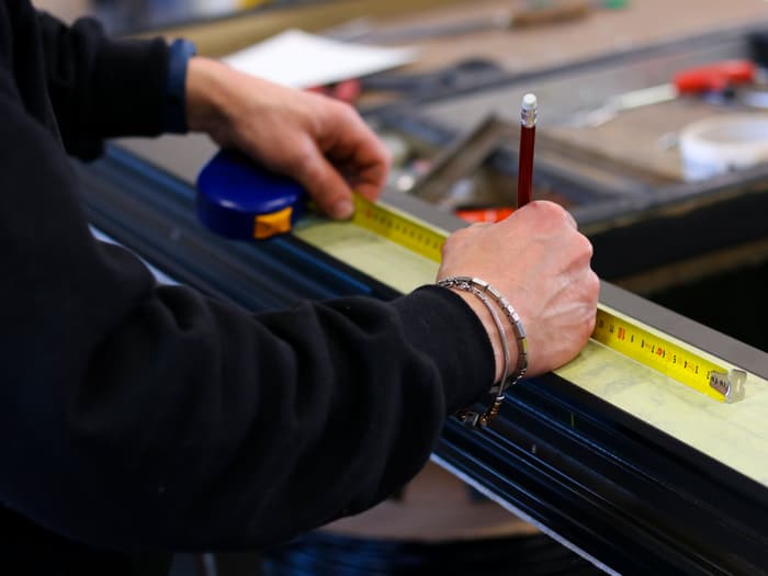 Zwei Hände messen ein Metallprofil mit dem Bandmaß und markieren es mit einem Bleistift