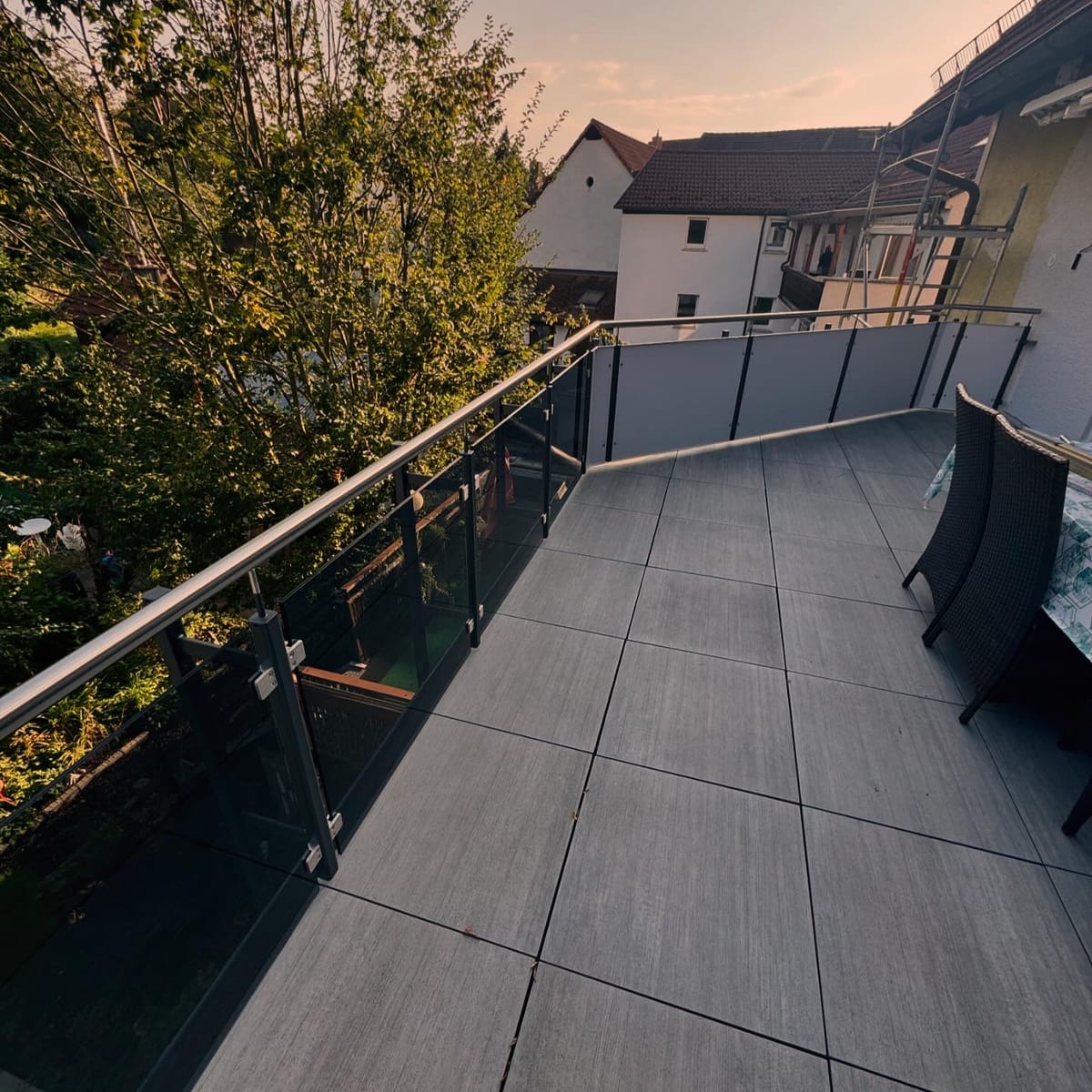 Dachterrasse mit Glasgeländer und durchlaufendem Edelstahl-Handlauf, dahinter der Blick über die Nachbardächer im Abendlicht